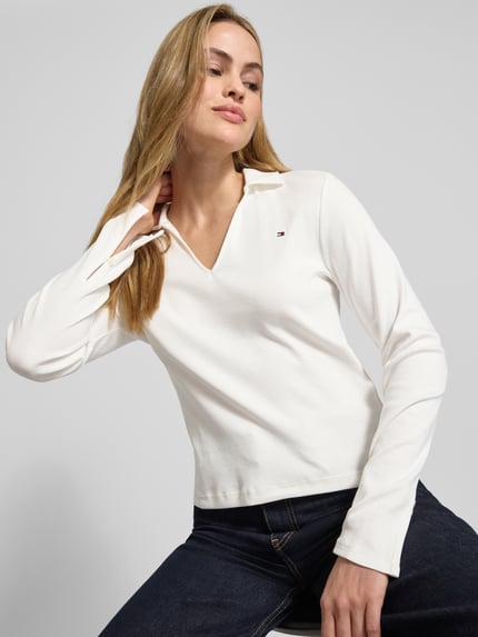 Frauenmodel trägt Slim Fit Langarmshirt aus reiner Baumwolle von Tommy Hilfiger in Unifarbe mit Logo-Detail, Nahaufnahme Oberkörper.
