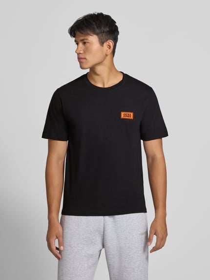 Męski model nosi Regular Fit T-Shirt aus reiner Baumwolle mit Label-Detail von JACK & JONES, czarny, okrągły dekolt, kontekst: męska koszulka, 100% bawełny, krój regular fit, detal z logo, długość tyłu w rozmiarze M: 67 cm, Ganzkörperansicht von vorne.