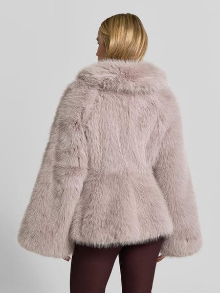 Frauenmodel trägt Flared Jacke aus Kunstfell von ROTATE in Hellrosa mit Trompetenärmeln, weich texturiert, Rückenansicht, Ganzkörperansicht von hinten. Innenfutter mit Viskose-Anteil, gerade Passform, Rückenlänge 60 cm, Brustweite 39 cm, Ärmellänge 66 cm bei Größe 36.