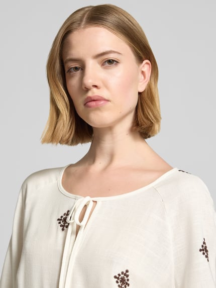 Frauenmodel trägt Bluse aus Viskose-Mix mit 3/4-Arm von Christian Berg Woman Selection in Creme mit Stickerei, Nahaufnahme Oberkörper. Leichte Struktur, Schlüsselloch-Ausschnitt mit Schnürung, Straight Fit, elastischer Abschluss am Ärmel, Viskose-Mix mit Leinen-Anteil.