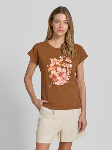 Frauenmodel trägt Damen T-Shirt mit Motiv-Print Modell 'RINA' von Soyaconcept in Braun, Baumwoll-Elasthan-Mix, Regular-Fit, Rundhalsausschnitt, Motiv-Print mit Blumen, Ärmel mit Aufschlag, Rückenlänge bei Größe S 61 cm, Ganzkörperansicht von vorne.