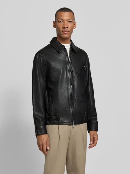 Męski model nosi Regular Fit Lederjacke aus Schafsleder von AllSaints, czarna, z zamkiem błyskawicznym dwustronnym, kieszeń na piersi, kieszenie boczne, Model 'arto', kołnierzyk typu kent, skóra owcza, Ganzkörperansicht von vorne
