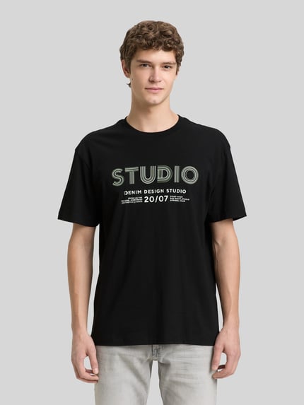 Mannenmodel draagt Relaxed Fit T-Shirt uit pure katoen van Tom Tailor Denim, uni zwart met labelprint, ronde hals, korte mouw, frontale full-body opname.