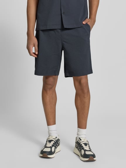 Männermodel trägt Loose Fit Shorts aus Baumwoll-Mix von Lacoste, Optik:Allover-Muster, gestreift, Materialverarbeitung: Seersucker, Ganzkörperansicht von vorne.
