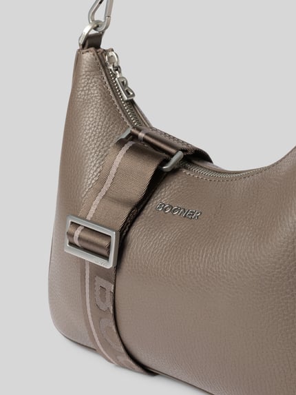 Produktfoto, Handtasche mit Schulterriemen Modell 'wallis odette' von BOGNER in Taupe, feine Narbung, Label-Applikation sichtbar, Detailaufnahme. Hauptfach mit Reißverschluss, Tragehenkel und Schulterriemen, Maße: 26x24x7 cm, Schulterriemenlänge 47 cm.