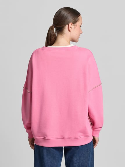 Frauenmodel trägt Oversized Sweatshirt aus reiner Baumwolle von miss goodlife in Rosa mit Pailettenbesatz, elastische Abschlüsse, Ganzkörperansicht Rückansicht.