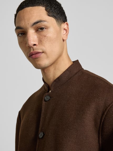 Männermodel trägt Hemdjacke mit Stehkragen von Officine Générale, braun, unifarben, sichtbare Knöpfe und strukturierte Filz-Oberfläche, Nahaufnahme Oberkörper.