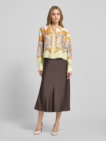 Modelka kobieca nosi Boxy Fit Bluse aus Satin im Allover-Look von Herzensangelegenheit, wzór w odcieniach żółci i brązu, satynowa tekstura, całkowity widok z przodu.