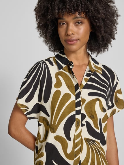 Vrouwenmodel draagt dames blouse Regular Fit Bluse aus Viskose mit Knotendetail Modell 'FELDI' van Soyaconcept in all-over look, zuiver viscose, overhemdkraag, verborgen knoopsluiting, knoopdetail, ruglengte maat S 54 cm, mouwlengte maat S 10 cm, zwart-wit en olijfgroen abstract dessin. Nahaufnahme bovenlichaam.