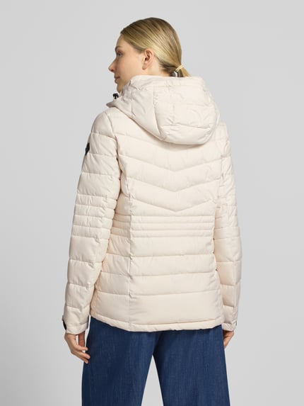 Frauenmodel trägt Jacke mit Kapuze und Label-Patch Modell von G.I.G.A. DX in Beige mit gestepptem Muster, Ganzkörperansicht Rückansicht.