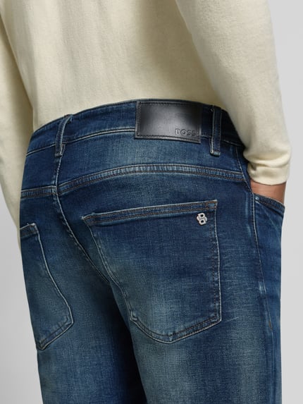 Männermodel trägt Slim Fit Jeans mit Label-Patch Modell 'DELAWARE BO' von BOSS Orange, Denim in Medium Wash mit Used Look, Detailaufnahme Rückansicht.