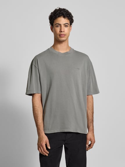 Männermodel trägt Oversized T-Shirt mit Label-Stitching von Pegador in Grau, reine Baumwolle, gerippter Rundhalsausschnitt, Ganzkörperansicht von vorne.