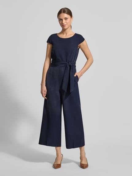 Kobiece modelka nosi Kombinezon mit Bindegürtel od Christian Berg Woman Selection, mieszanka materiałów z dodatkiem streczu, krój regular fit, okrągły dekolt, wiązany pasek, długość tyłu w rozmiarze 36: 39 cm, szerokość w rozmiarze 36: 37 cm, długość rękawów w rozmiarze 36: 7 cm, całkowita długość w rozmiarze 36: 130 cm, długość wewnętrzna nogawki w rozmiarze 36: 61 cm, ciemnoniebieski, gładka tekstura, szerokie nogawki, pełny widok z przodu