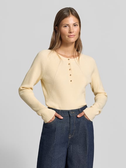 Frauenmodel trägt Slim Fit Longsleeve aus Strick-Optik von MYON, cremefarben, Knopfleiste, Rundhalsausschnitt, Ganzkörperansicht von vorne.