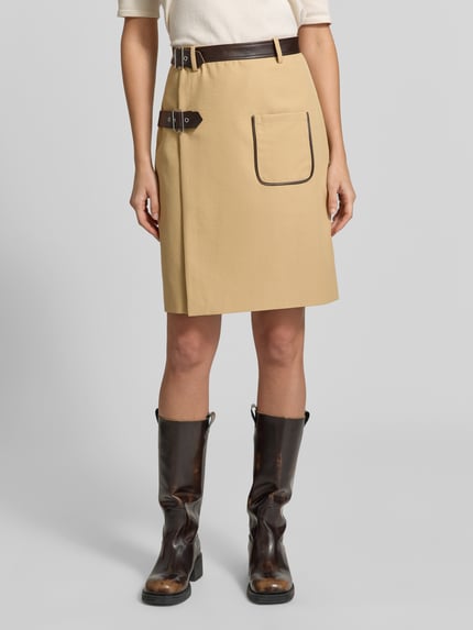 Frauenmodel trägt Midi-Rock mit Doppelgurt Modell 'SVEA' von BAUM & PFERDGARTEN, beige, Wickeloptik, Lederoptik, Schnalle, Ziertasche, Ganzkörperansicht von vorne.