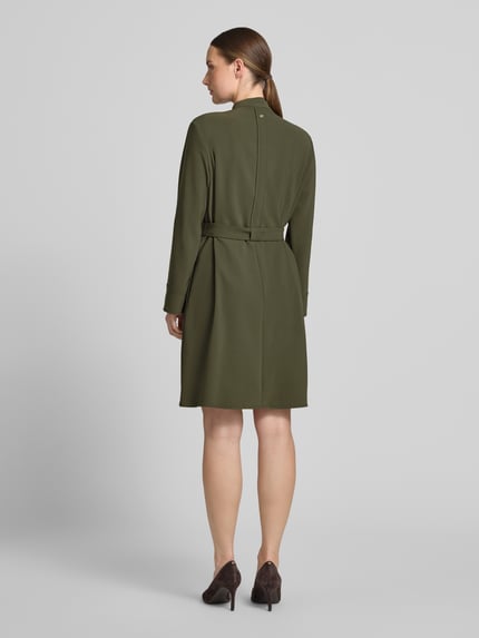 Frauenmodel trägt Knielanges Kleid mit Stehkragen und Gürtel von Marc Cain in Olivgrün, Material-Mix mit Stretch-Anteil, taillierter Schnitt, Rückenlänge 94 cm, Ärmel 58 cm, Ganzkörperansicht Rückansicht