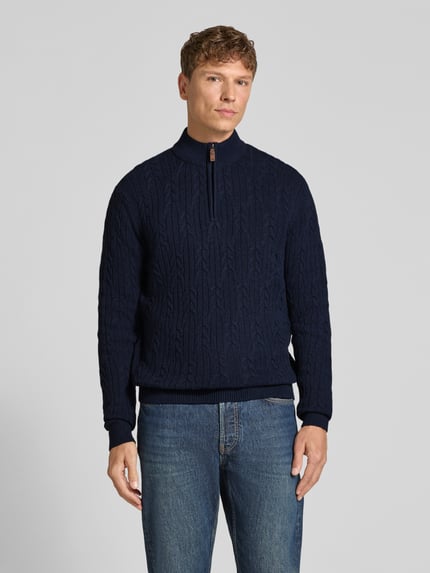 Männermodel trägt dunkelblauen Slim Fit Strickpullover aus Baumwoll-Woll-Mix von Fynch-Hatton mit Zopfmuster und Troyer-Kragen, Ganzkörperansicht von vorne.