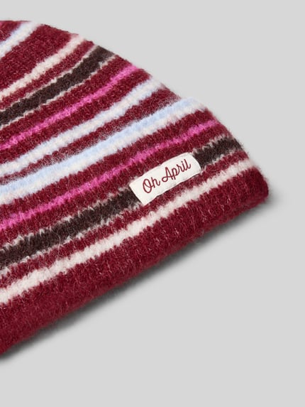 Produktfoto, Beanie met labeldetail model 'Arlo' van OH APRIL, materiaalmix met wol, brede krempel, gestreepte structuur in rood, roze en wit