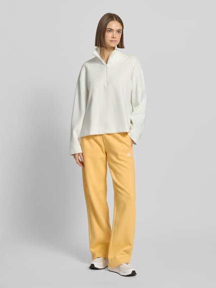 Modelka kobieca nosi Pullover mit Stehkragen und Reißverschluss od adidas Sportswear, biały, z poliestru, luźny krój, logo, widok całej sylwetki z przodu.