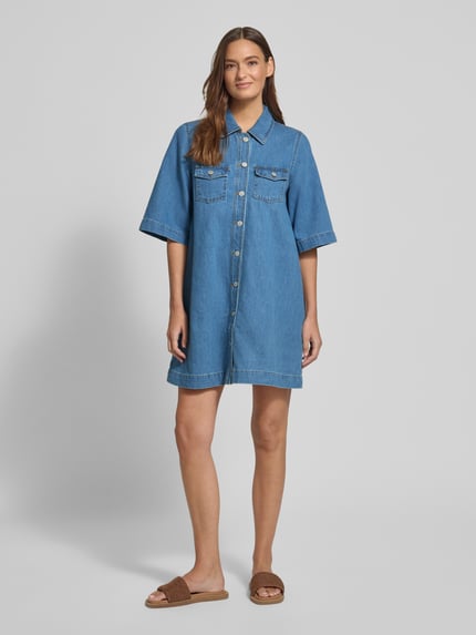 Modelka nosi Jeanskleid mit Brusttaschen Modell 'Mira' von mbyM z bawełny, krój relaxed fit, sukienka mini z kołnierzykiem koszulowym, kieszenie na piersi, listwa guzikowa, długość tyłu w rozmiarze S: 89 cm, szerokość w rozmiarze S: 43 cm, długość rękawów w rozmiarze S: 34 cm, niebieski denim, miękka faktura, widok całej sylwetki z przodu.