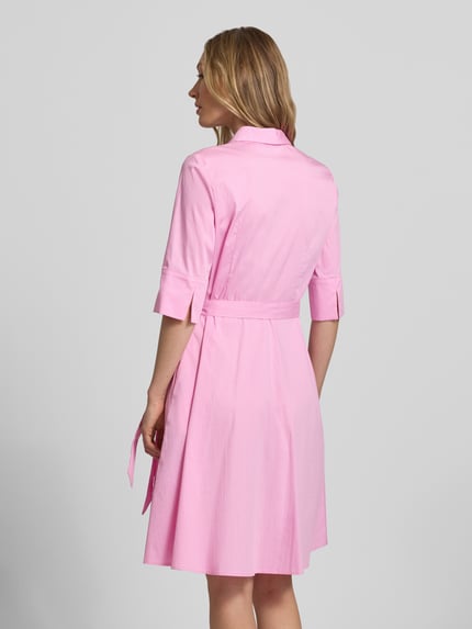 Vrouwenmodel draagt Knielanges Hemdblusenkleid met Bindegürtel van Christian Berg Woman Selection, katoenmix met stretch, a-lijn, knielengte, verborgen knoopsluiting, strikceintuur, ruglengte maat 36: 99 cm, borstwijdte maat 36: 48 cm, mouwlengte maat 36: 37 cm, effen roze, gladde stofstructuur. Ganzlichaansicht achteraan.