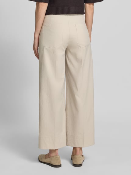 Frauenmodel trägt Stoffhose mit Eingrifftaschen Modell 'CARA' von Cambio in Beige mit Wide-Fit, Haken- und Reißverschluss, Ganzkörperansicht Rückansicht.