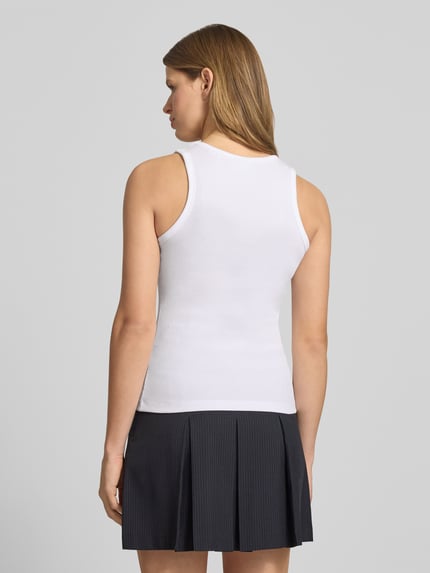 Kobiece modelka nosi biały top z efektem prążkowania, mieszanka bawełny i elastanu, krój slim fit, model 'FRIDA' od JJXX, długość tyłu 54 cm w rozmiarze S, widok całej sylwetki z tyłu.