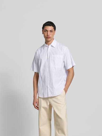 Męski model nosi Classic Fit Freizeithemd aus Baumwolle od ANNARR, białe z pionowymi paskami, brustasza, krótki rękaw, koszula casualowa, listwa guzikowa na całej długości, długość tyłu w rozmiarze M: 81 cm, szerokość ramion w rozmiarze M: 48 cm, długość rękawów w rozmiarze M: 28 cm. Ganzkörperansicht von vorne.