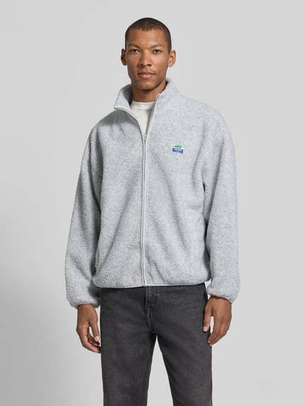 Männermodel trägt Sweatjacke Modell 'HOKTOWN' mit Logo-Patch von AMERICAN VINTAGE in Hellgrau, Struktur, Regular Fit, Longline, Ganzkörperansicht von vorne.