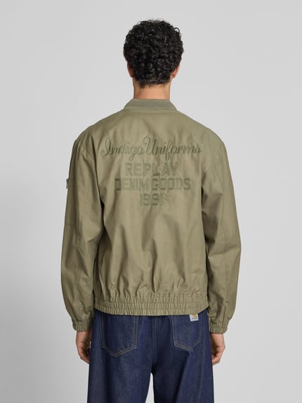 Männermodel trägt Bomberjacke mit Reißverschlusstasche am Ärmel von Replay aus Baumwoll-Mix, Gerader-Schnitt, Rückenlänge 68 cm, Ganzkörperansicht Rückansicht.