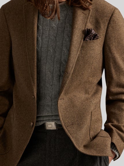 Männermodel draagt Regular Fit Anzugsakko met wol-aandeel van Polo Ralph Lauren in melange-look, reverskraag, label-applicatie, grijze trui, eenknoopssluiting, lange mouw, detailopname bovenlichaam.