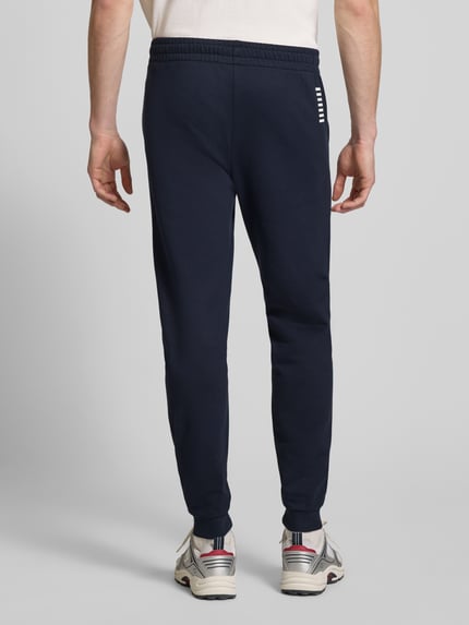 Männermodel trägt Sweatpants mit Logo und elastischem Bund von EA7 Emporio Armani in Dunkelblau, Regular Fit, Ganzkörperansicht Rückansicht.