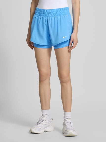 Vrouwenmodel draagt Regular Fit Shorts met Integrierten Tights van NIKE TRAINING in lichtblauw, elastische materiaalmix, voorkant volledig, regular fit, geïntegreerde tights, elastische band, bandwijdte maat S 37 cm, binnenbeenlengte maat S 8 cm, nahaufnahme onderlichaam.