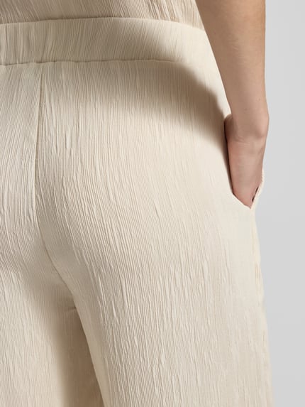 Kobiece modelka nosi spodnie materiałowe Wide Fit z mieszanki wiskozy model 'Mucia' od OPUS PANTS, fakturowany wzór, kolor kremowy, z elastycznym pasem, detaliczne zbliżenie na biodra i kieszeń.