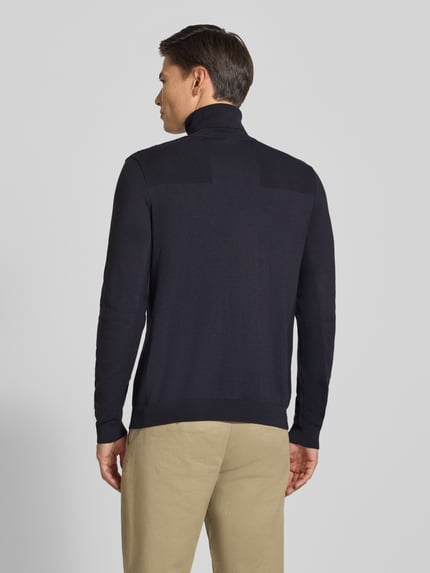 Männermodel trägt Regular Fit Rollkragenpullover aus Woll-Mix von BOSS in unifarbener Strickoptik mit Strukturmuster, Ganzkörperansicht Rückansicht.