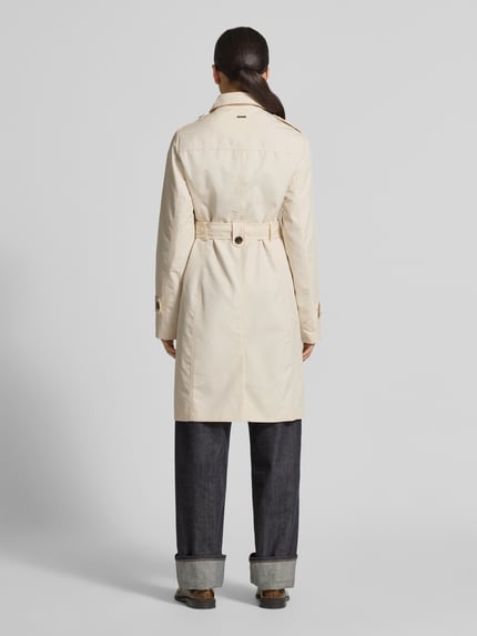 Vrouwenmodel draagt Regular Fit Trenchcoat aus Baumwoll-Mix van s.Oliver RED LABEL in effen beige twill met schouderstukken, riemlussen en dubbele knoopsluiting, lange mouwen, klepzakken, rugpas, achterkant volledig zichtbaar, volledige lichaamsaanzicht rugzijde.
