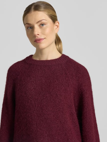 Vrouwenmodel draagt Strickpullover mit Raglanärmeln van FREE/QUENT in bordeauxrood, rechte fit, ronde hals, materiaal met wol, nahaufnahme bovenlichaam.