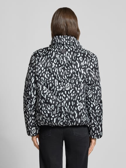 Frauenmodel trägt Regular Fit Daunenjacke mit Wendefunktion von Marc Cain für Damen, schwarz mit weißem Muster, Ganzkörperansicht Rückansicht.