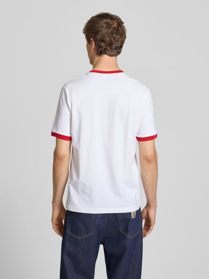 Männermodel trägt weißes T-Shirt mit Rundhalsausschnitt und Label-Stitchings von CHAMPION, rote Akzente, Regular Fit, Ganzkörperansicht Rückansicht.