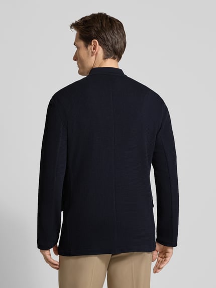 Männermodel trägt Slim Fit Sakko mit Stehkragen und Pattentaschen von Emporio Armani, dunkle Farbe, Material-Mix mit Viskose-Anteil, Ganzkörperansicht Rückansicht.