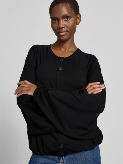 Vrouwenmodel draagt Oversized Cardigan aus Lyocell-Mix van black palms in zwart met ronde hals, knoopsluiting, elastische boorden, oversized fit, ruglengte bij maat S/M 58 cm, mix van lyocell, frontale close-up van bovenlichaam.