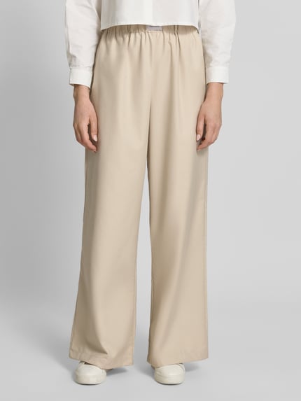 Frauenmodel trägt Wide Leg Hose aus Viskose-Mix Modell 'TOSCA' von VILLA SOPHIE in Optik: Unifarben mit seitlichen Eingrifftaschen, Bundabschluss: elastisch, Passform: Wide-Leg, Material: Viskose-Mix, beige, glatte Textur, Ganzkörperansicht von vorne.