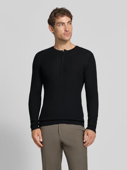 Männermodel trägt Strickpullover aus Lyocell-Woll-Mix mit Knopfleiste von Antony Morato, Slim Fit, Ripp-Optik, schwarze Farbe, Ganzkörperansicht von vorne.