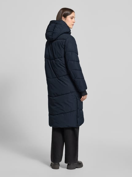 Frauenmodel trägt Steppmantel mit Reißverschlusstaschen von Amber & June in Dunkelblau, wattiert, matte Oberfläche, Ganzkörperansicht Rückansicht. Rückenlänge 111 cm, Regular Fit, Kapuze mit Tunnelzug, Reißverschlusstaschen, verdeckter Reißverschluss, Schulterbreite 40 cm, Brustweite 53 cm, Ärmellänge 69 cm.