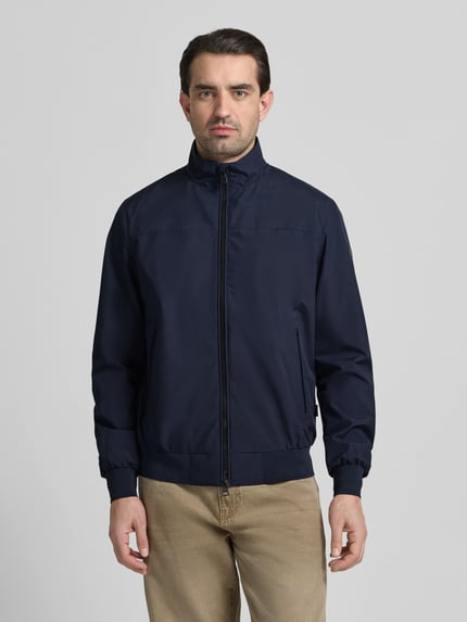 Mężczyzna nosi Regular Fit Jacke mit Stehkragen Modell 'Finlay' od SAVE THE DUCK, granatowa, gładka tekstura, przód, ujęcie całopostaciowe. Kontekst: męska kurtka, stójka, krój regular fit, dwukierunkowy zamek, kieszenie boczne na zamek, elastyczne wykończenia, długość pleców w rozmiarze M: 69 cm, szerokość ramion w rozmiarze M: 46 cm, szerokość w rozmiarze M: 60 cm, długość rękawa w rozmiarze M: 68 cm.