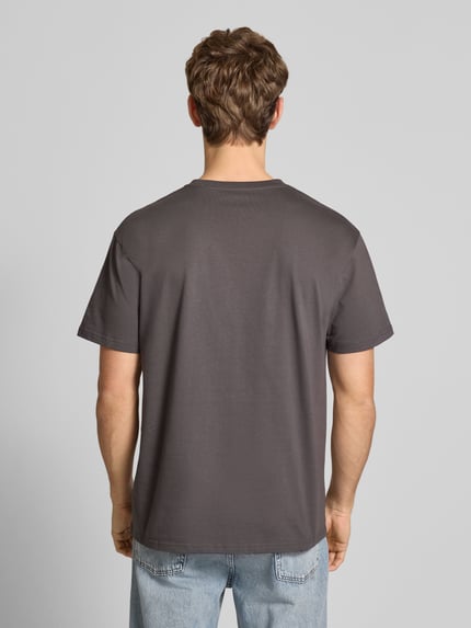 Männermodel trägt T-Shirt mit Label-Stitching Modell 'CHASE' von Carhartt, reine Baumwolle, Regular Fit, Rückenansicht, Ganzkörperansicht.