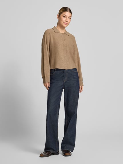 Frauenmodel trägt beigefarbene Regular Fit Strickjacke aus reiner Wolle Modell 'Dulena' von OPUS zu weiter Jeans, Ganzkörperansicht von vorne. Damen Pullover von OPUS.