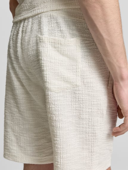 Männermodel trägt Shorts mit elastischem Bund von MCNEAL aus Material-Mix mit Baumwoll-Anteil, Strukturmuster, Nahaufnahme Oberschenkel.