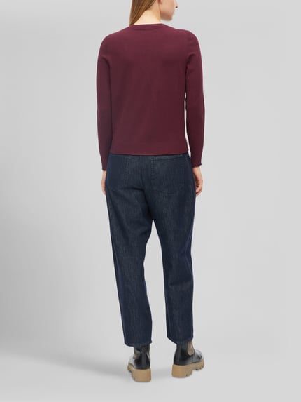 Frauenmodel trägt Slim Fit Pullover aus Viskose-Mix von s.Oliver RED LABEL in Dunkelrot zu dunkelblauer Hose, Ganzkörperansicht Rückansicht.