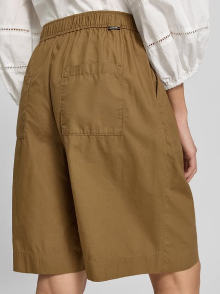 Kobieta nosi Relaxed Fit Bermuda aus reiner Baumwolle od s.Oliver RED LABEL w kolorze brązowym, gładka tekstura, widok całej sylwetki z tyłu.